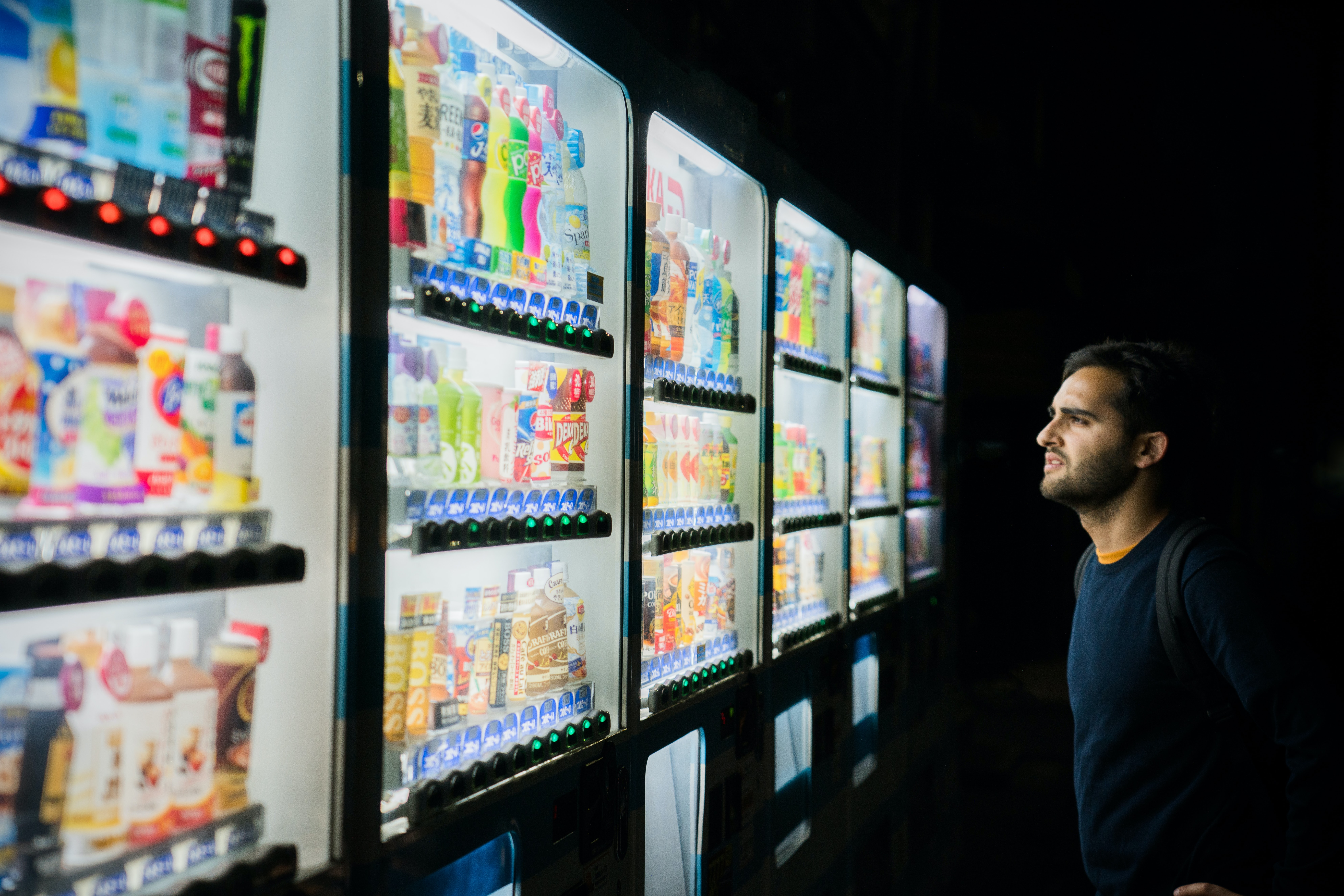 Imagem de um homem olhando para geladeiras cheias de bebidas em um supermercado.